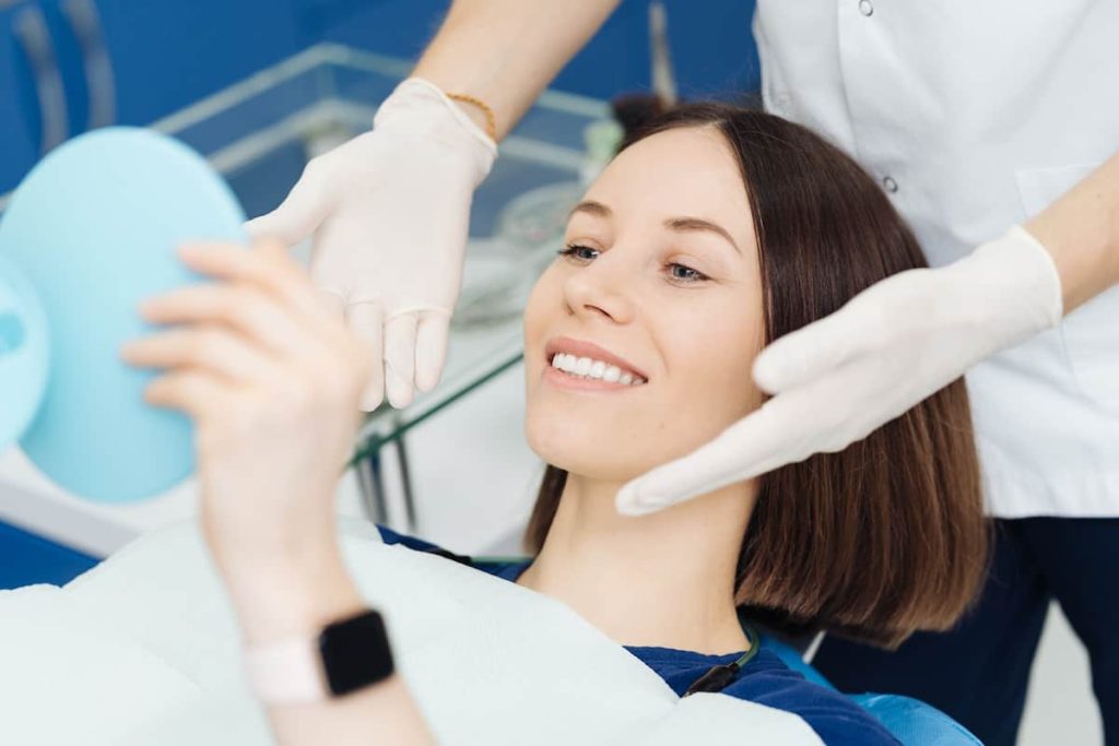 Patient admiring her Hollywood smile in a hand mirror at a Vancouver dental clinic